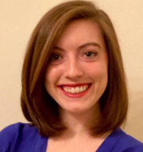 Emily Baldwin, a white woman with shoulder-length brown hair, wearing a blue top and smiling.