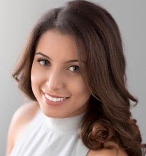 Yousra Hebeishy, a Moroccan woman with long dark brown hair, looking slightly upward toward the camera and smiling.