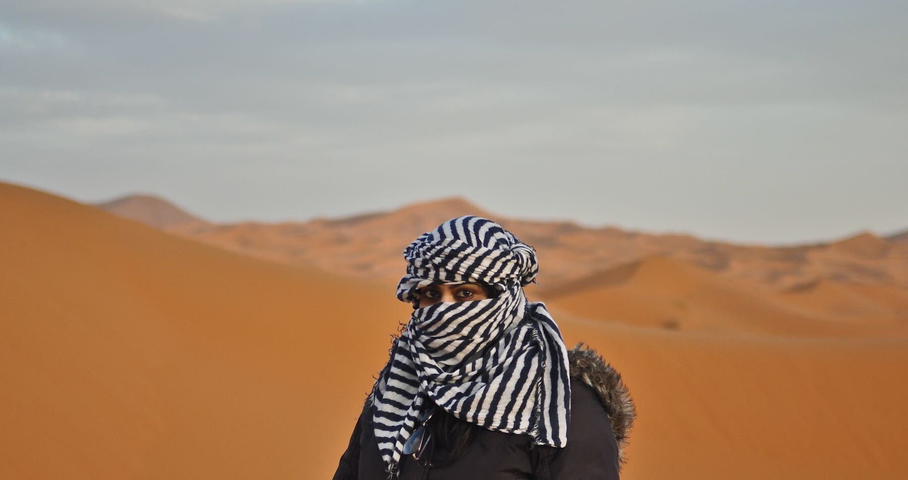 Maduri Asokan, an Indian woman, stands in the desert wearing a black-and-white striped headscarf.