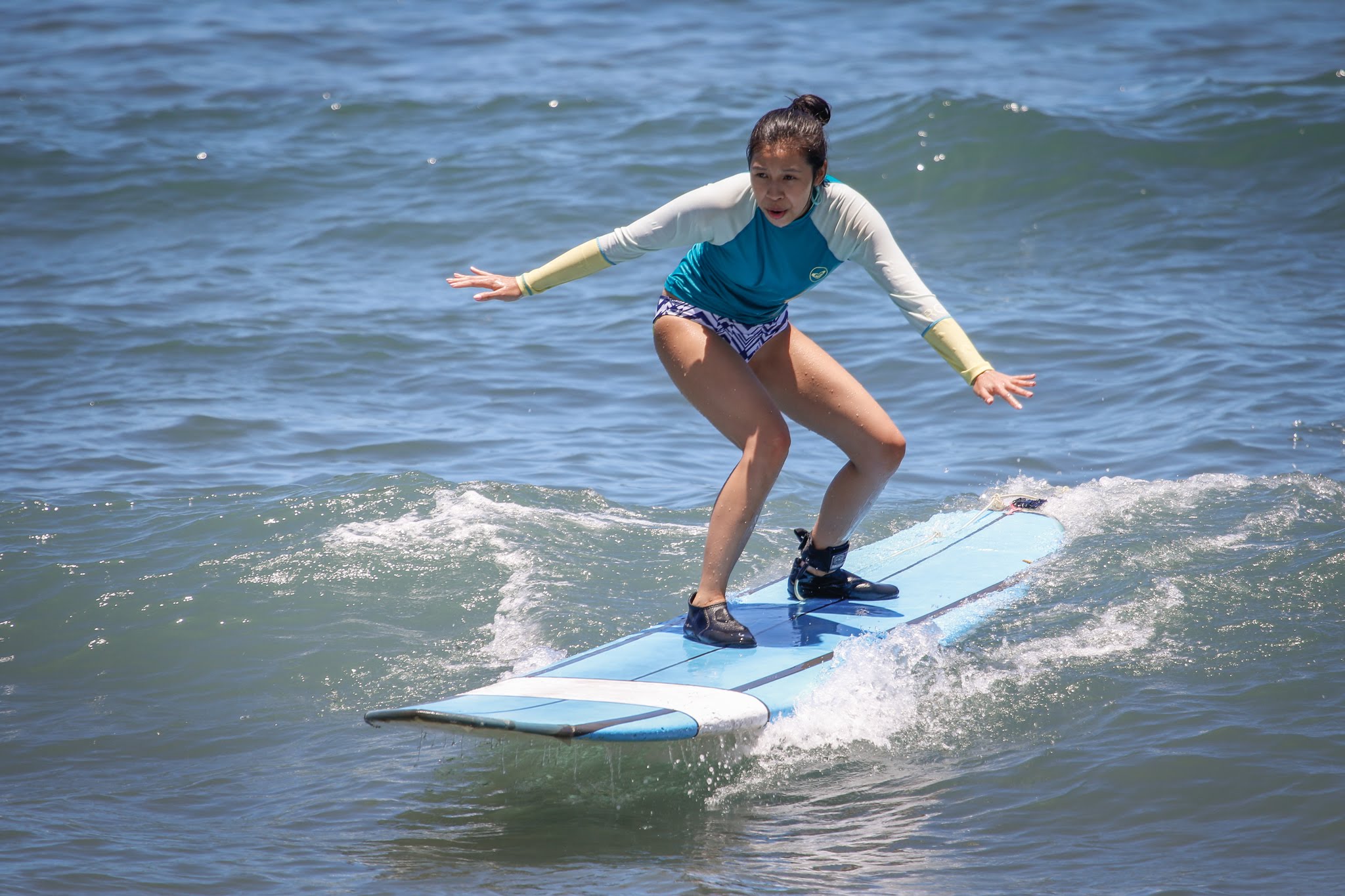 Tiffany Chin, a Chinese-American woman, holds her arms out as she rides a surfboard.